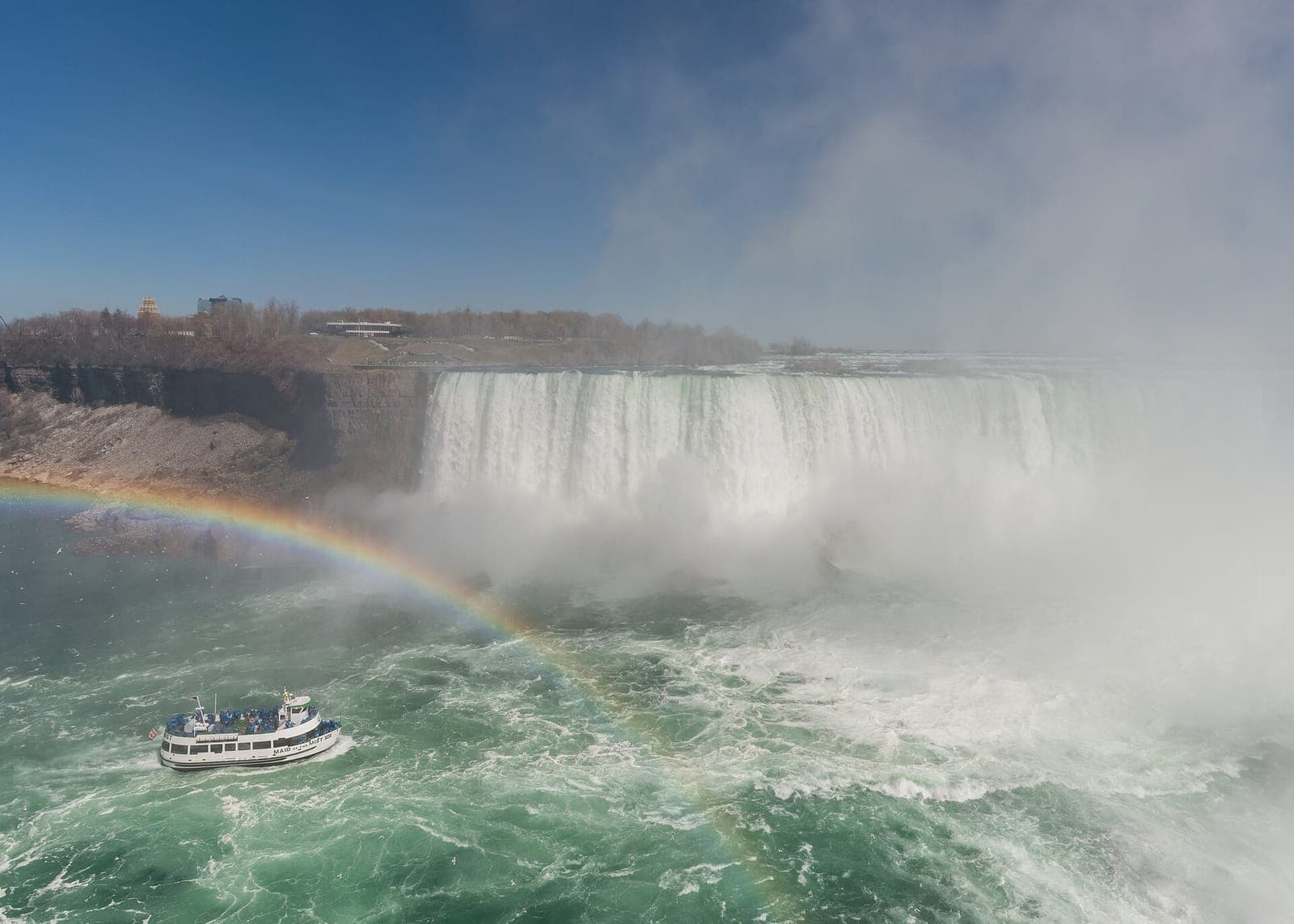 A Maid of the Mist boat below Niagara Falls with a rainbow